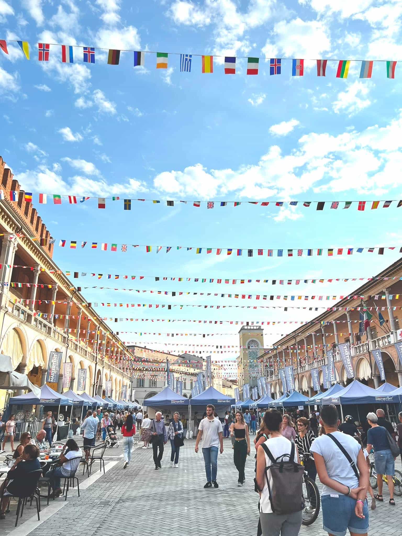 Festival stands and visitors at Argillà Italia in Faenza with rows of international flags overhead