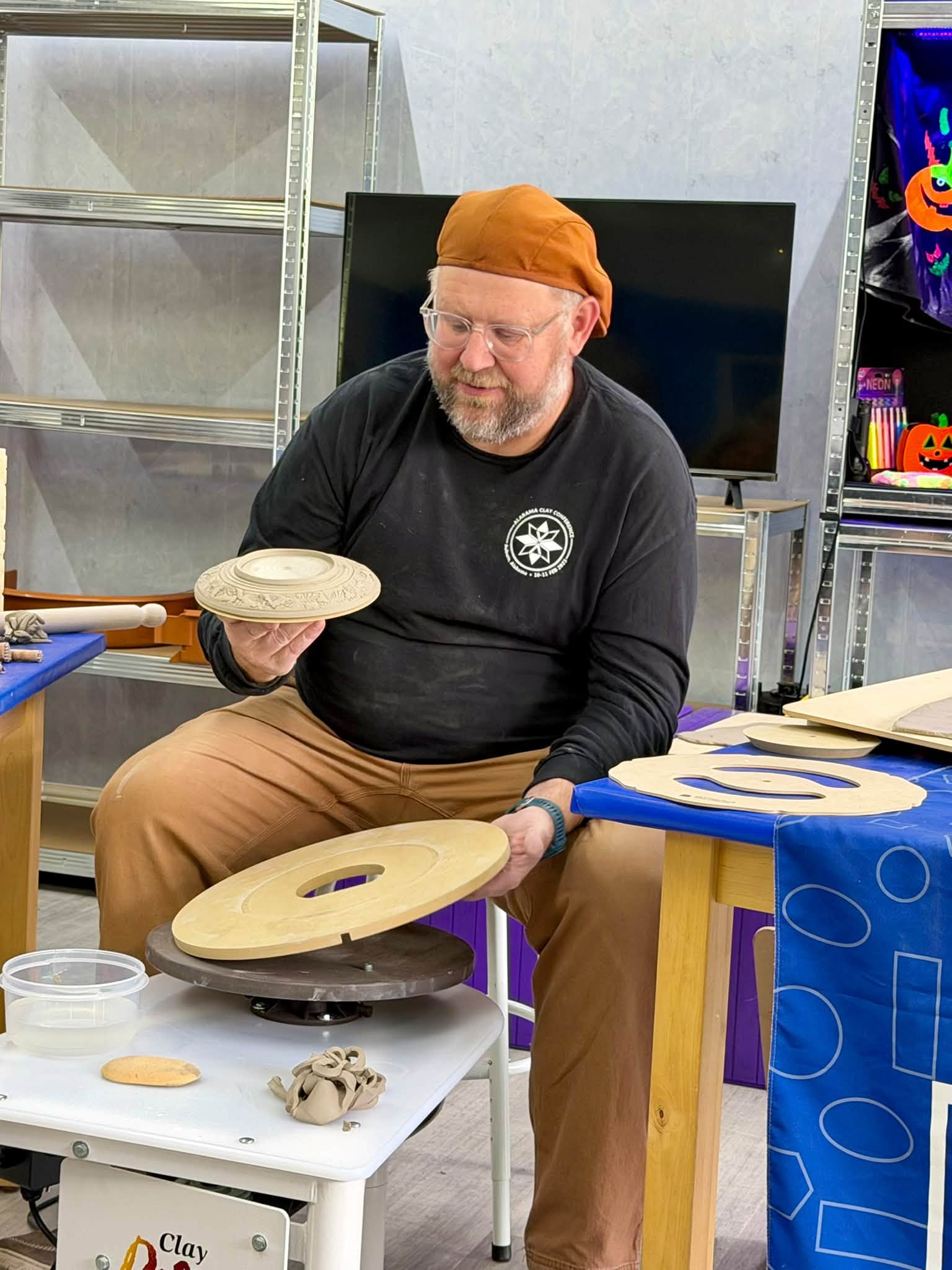 Jeff Rottman showing a finished clay piece beside GR Pottery Forms and a pottery wheel